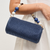 Blue woven handbag with a beaded strap held by a person against a white background