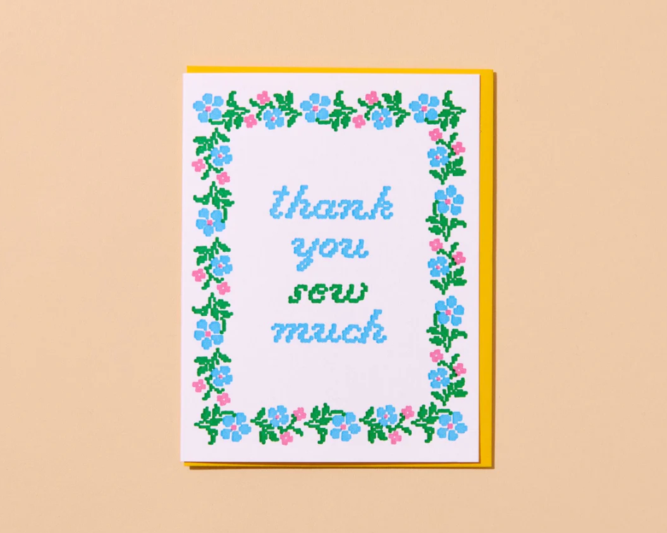 Framed cross-stitched art with 'thank you sew much' text on a beige background